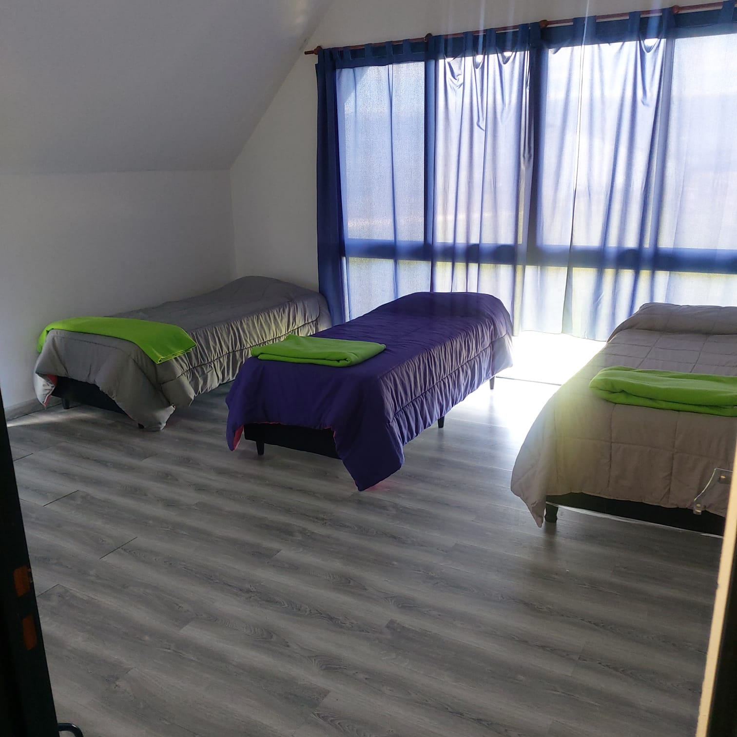 Dormitorio con tres camas individuales y cortinas azules
